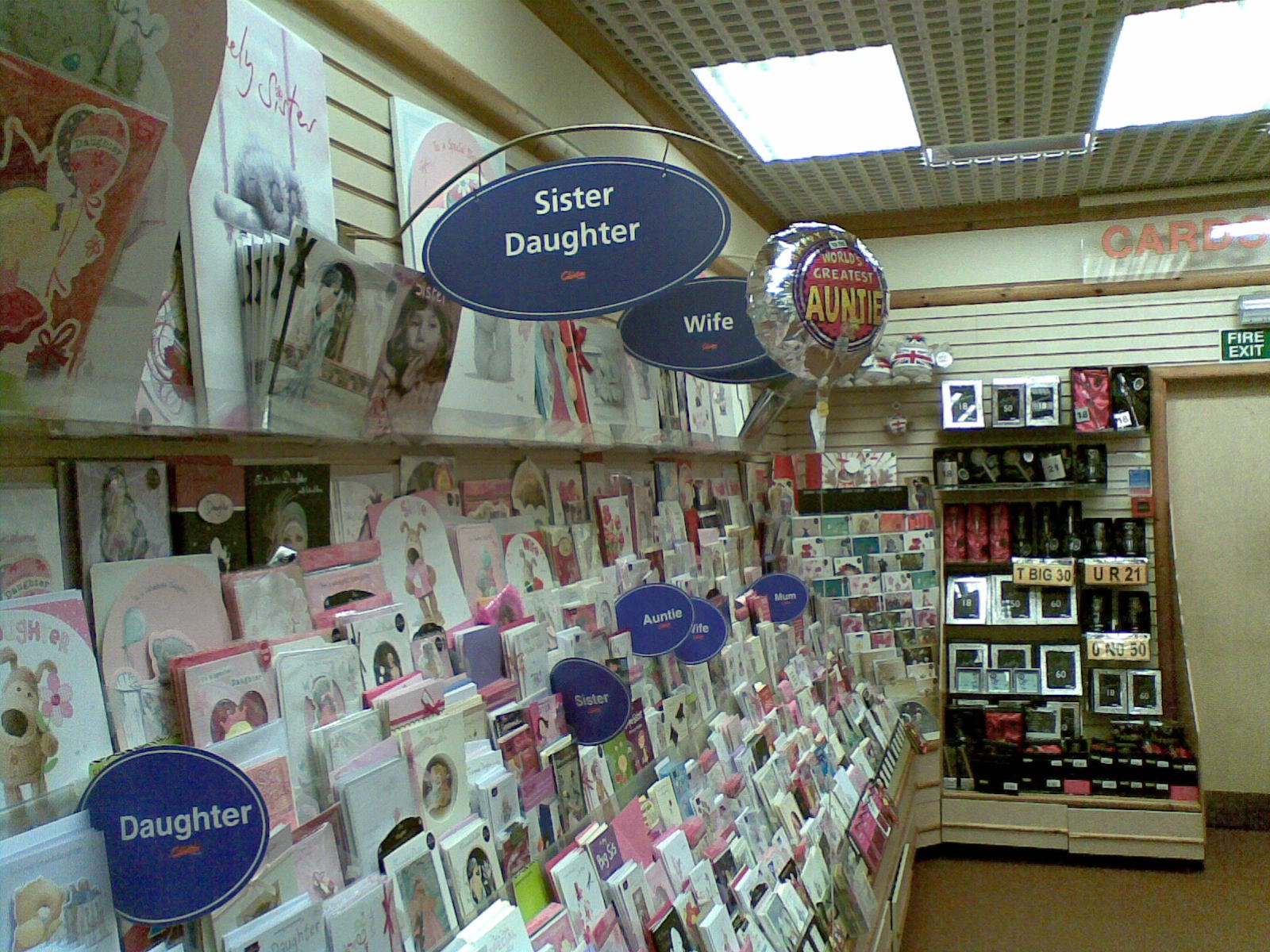 Photograph of the interior of a card shop, racks of greetings cards. Signs demarcating thematic groups of cards read "wife", "mum", "auntie", "sister daughter".